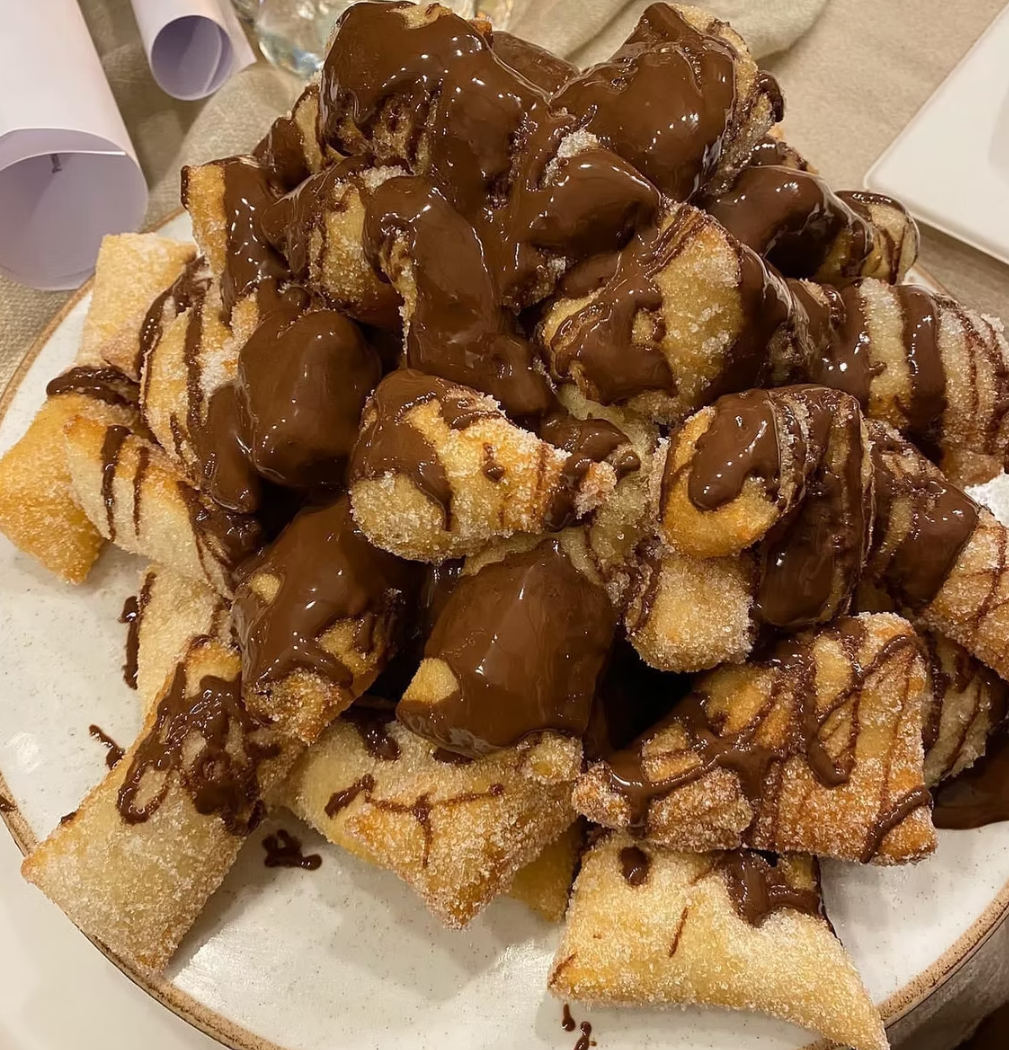 Pyramid of golden fried pastries drizzled with rich chocolate