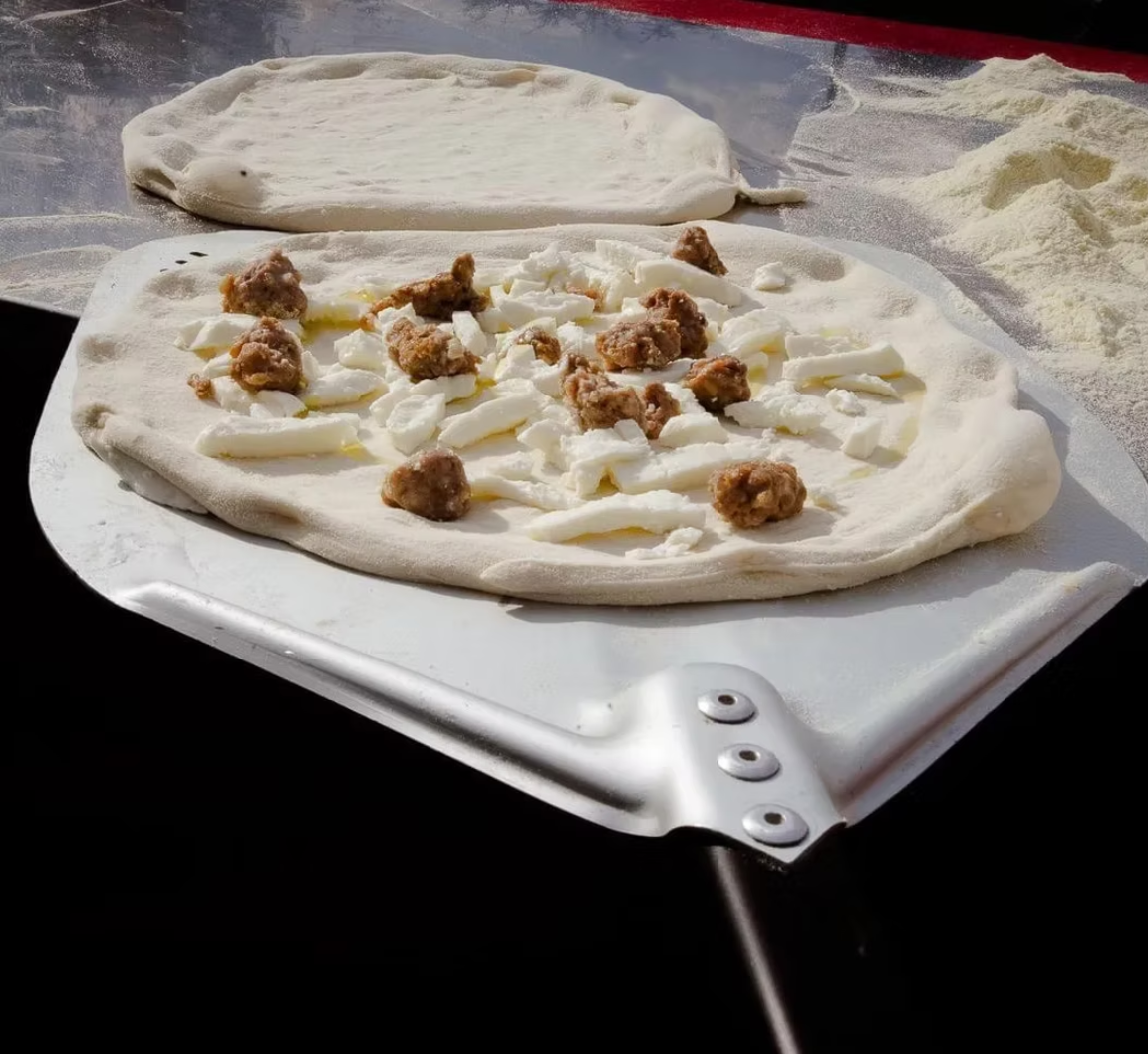 Pizza on peel with Italian sausage and fresh mozzarella