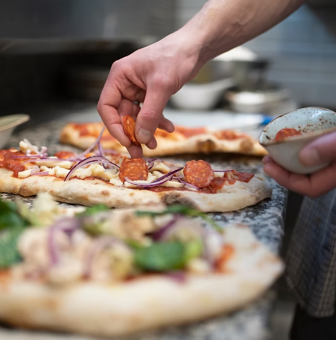 Chef hands placing pepperoni and red onion on artisanal pizza